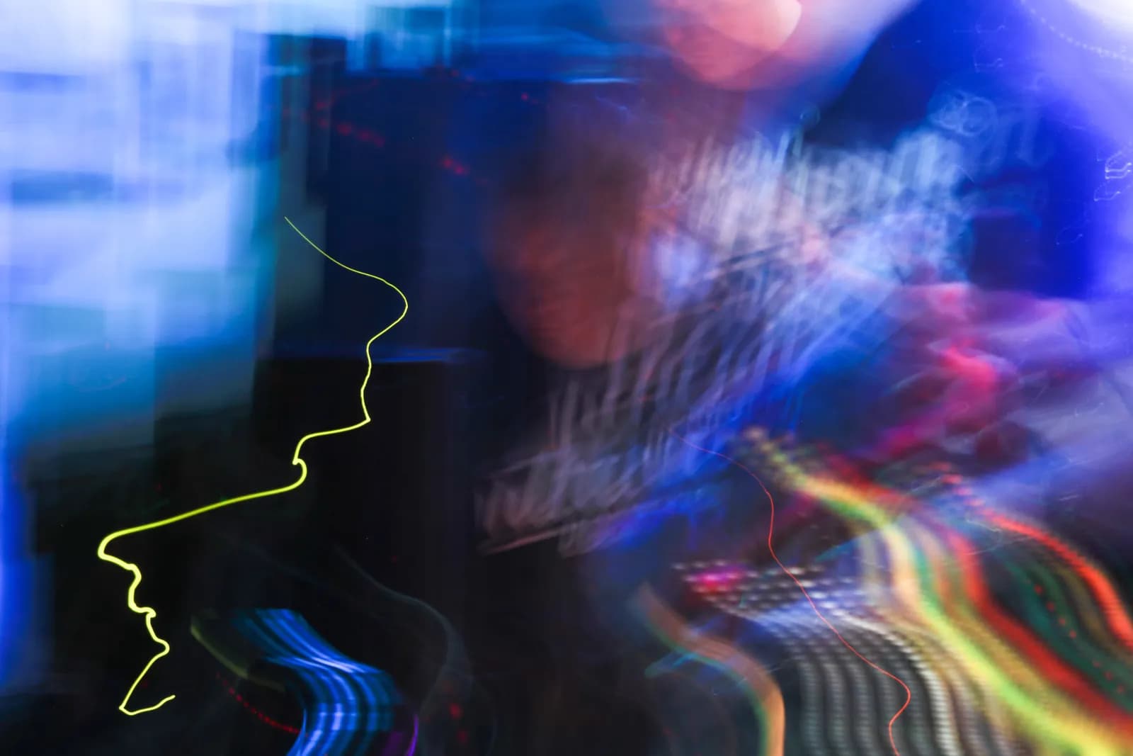 A long exposure photograph capturing vibrant light trails and blurred shapes in blue, green, yellow, and red hues, creating an abstract and dynamic composition.